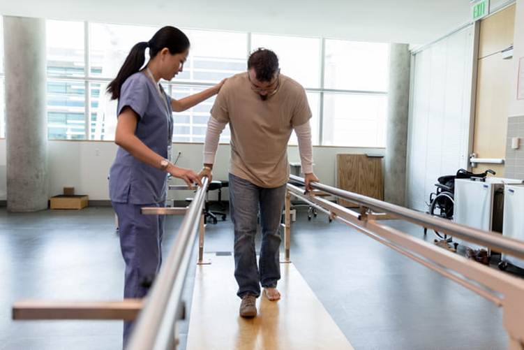 A physical therapist helps a patient walk after a brain injury.