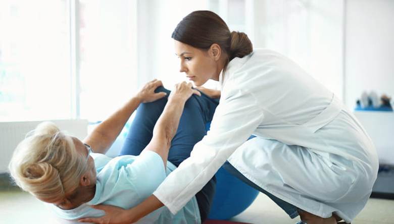 A physical therapist assists a patient as she does an exercise to help with back pain.